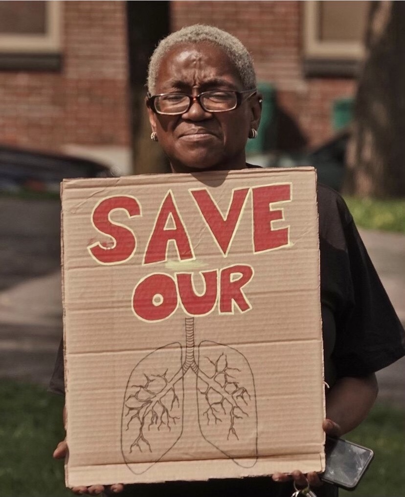 Neighborhood resident-Black female holding up a sign saying Save Our Lungs